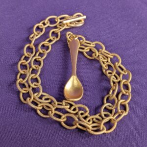 A necklace made of a gold plated textured chunky cable chain and a gold plated spoon pendant with a satin finish, secured with a toggle clasp